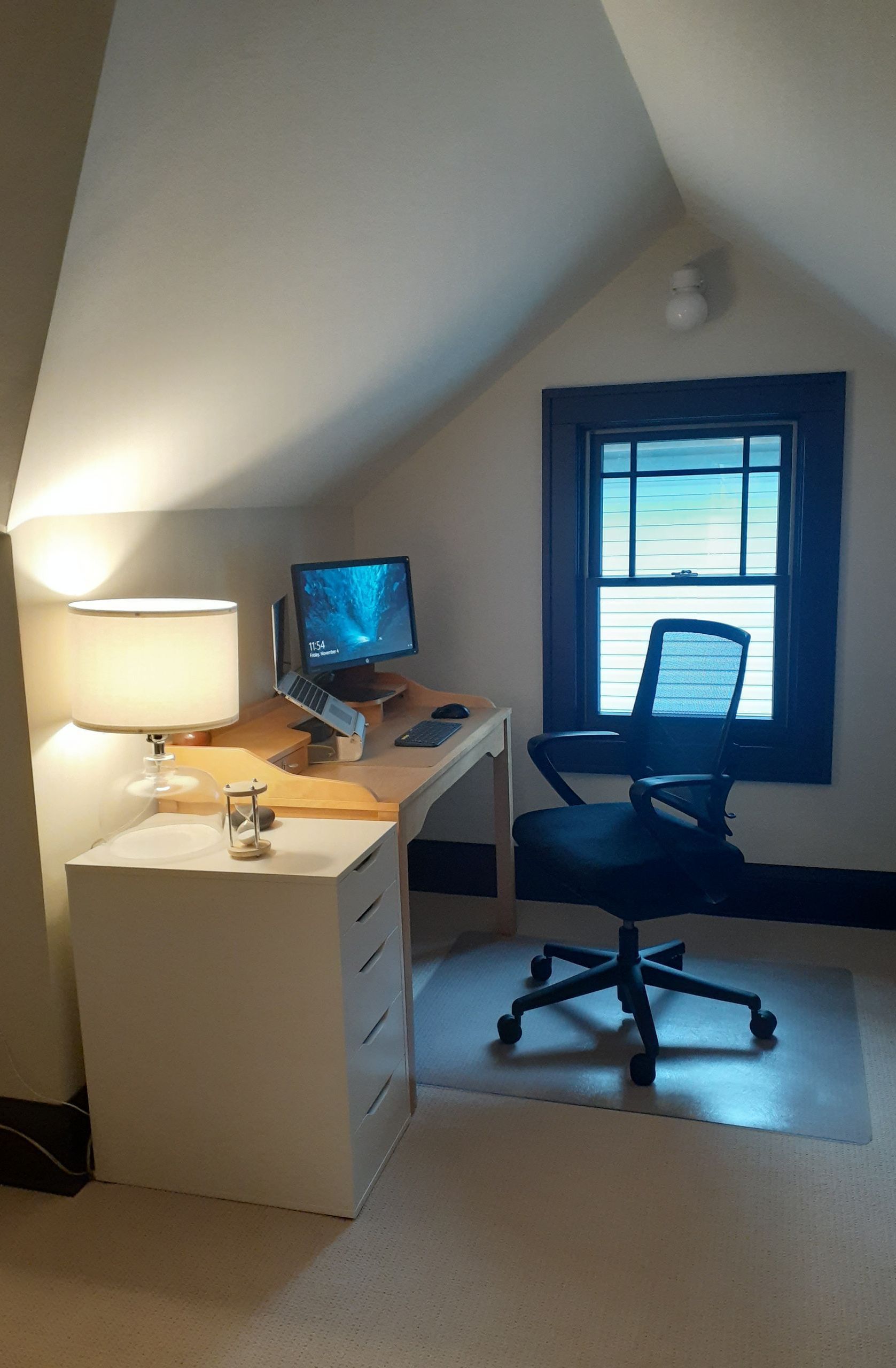 A room with a desk , chair , lamp and computer.