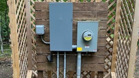 A electrical box with a meter attached to it is sitting on a wooden wall.