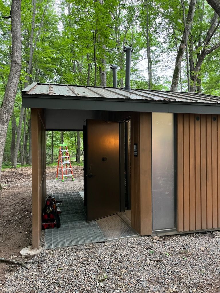 A small wooden building with a metal roof in the middle of a forest.