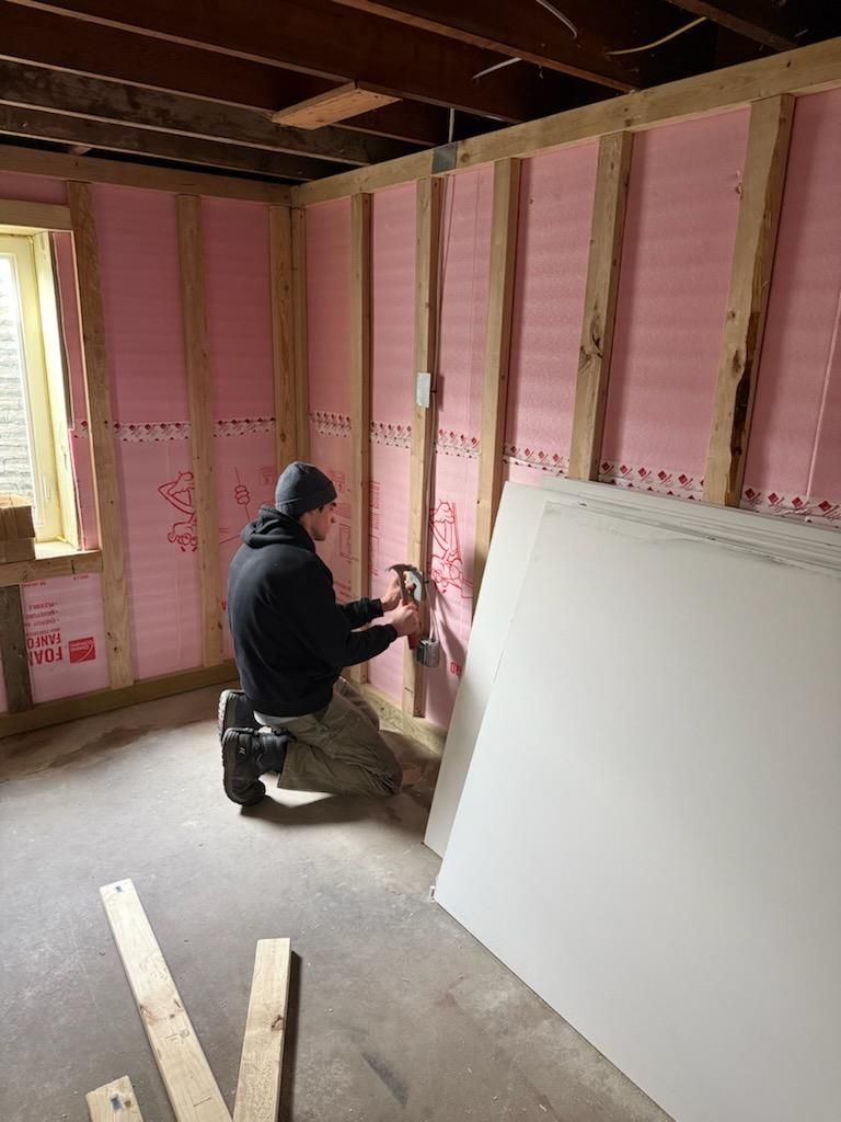 A man is working on a wall in a room with pink insulation.