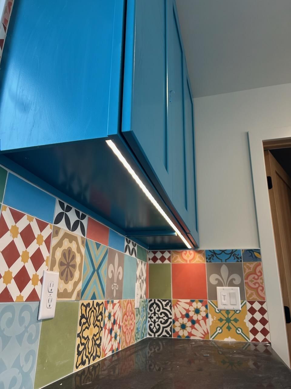 A kitchen with blue cabinets and colorful tiles on the wall