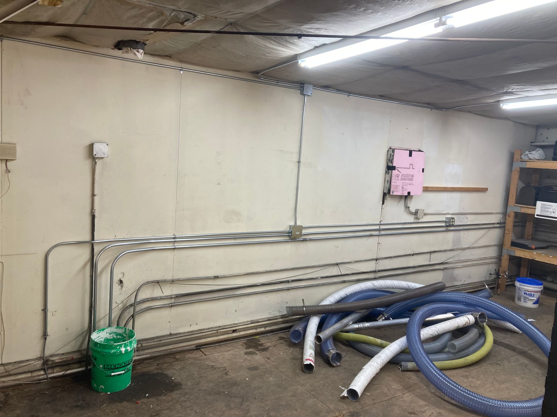 A room with a lot of pipes and a green bucket.