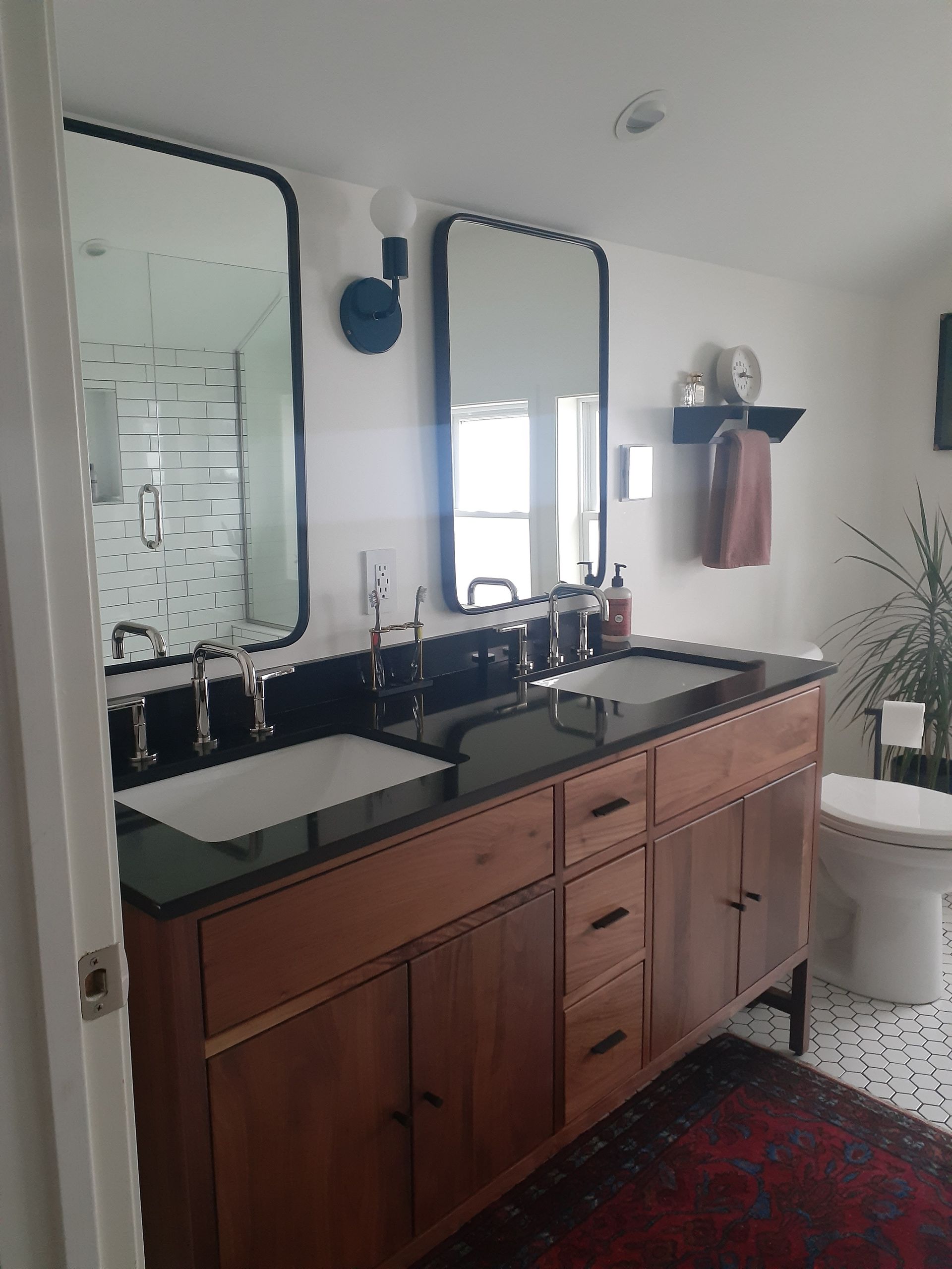 A bathroom with two sinks , two mirrors and a toilet.