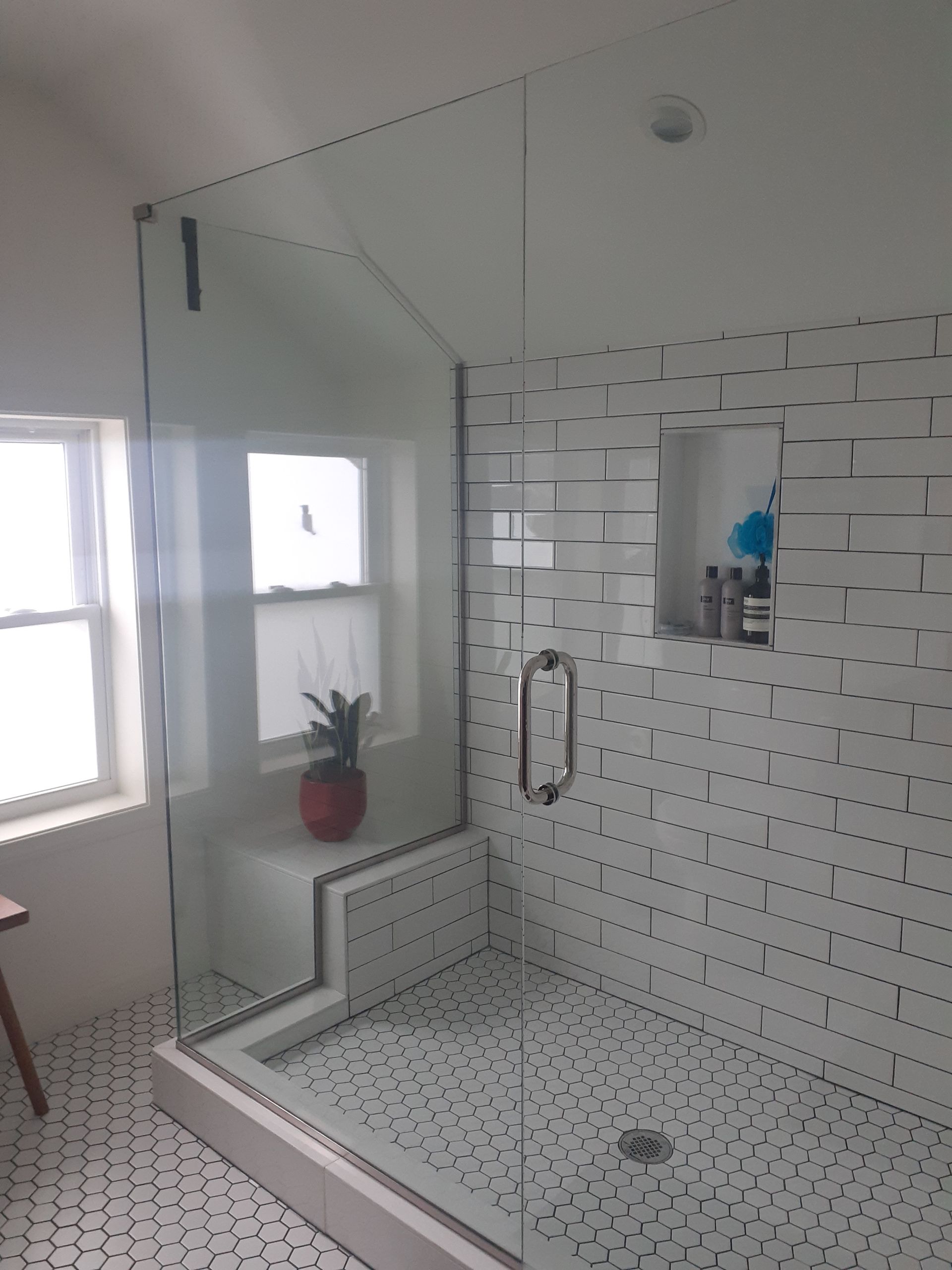 A bathroom with white tiles and a walk in shower with a glass door.