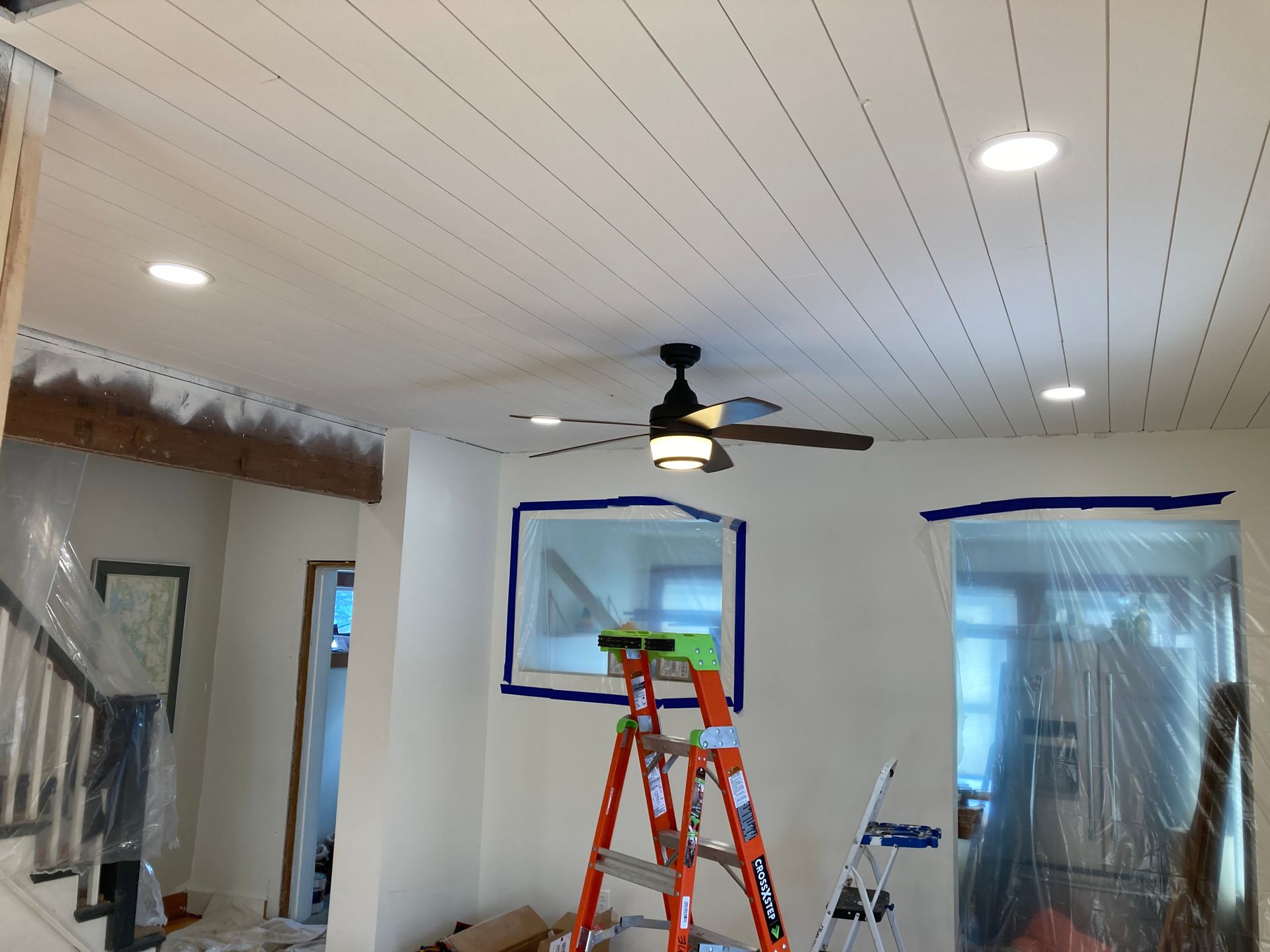 A living room with a ceiling fan and a ladder.