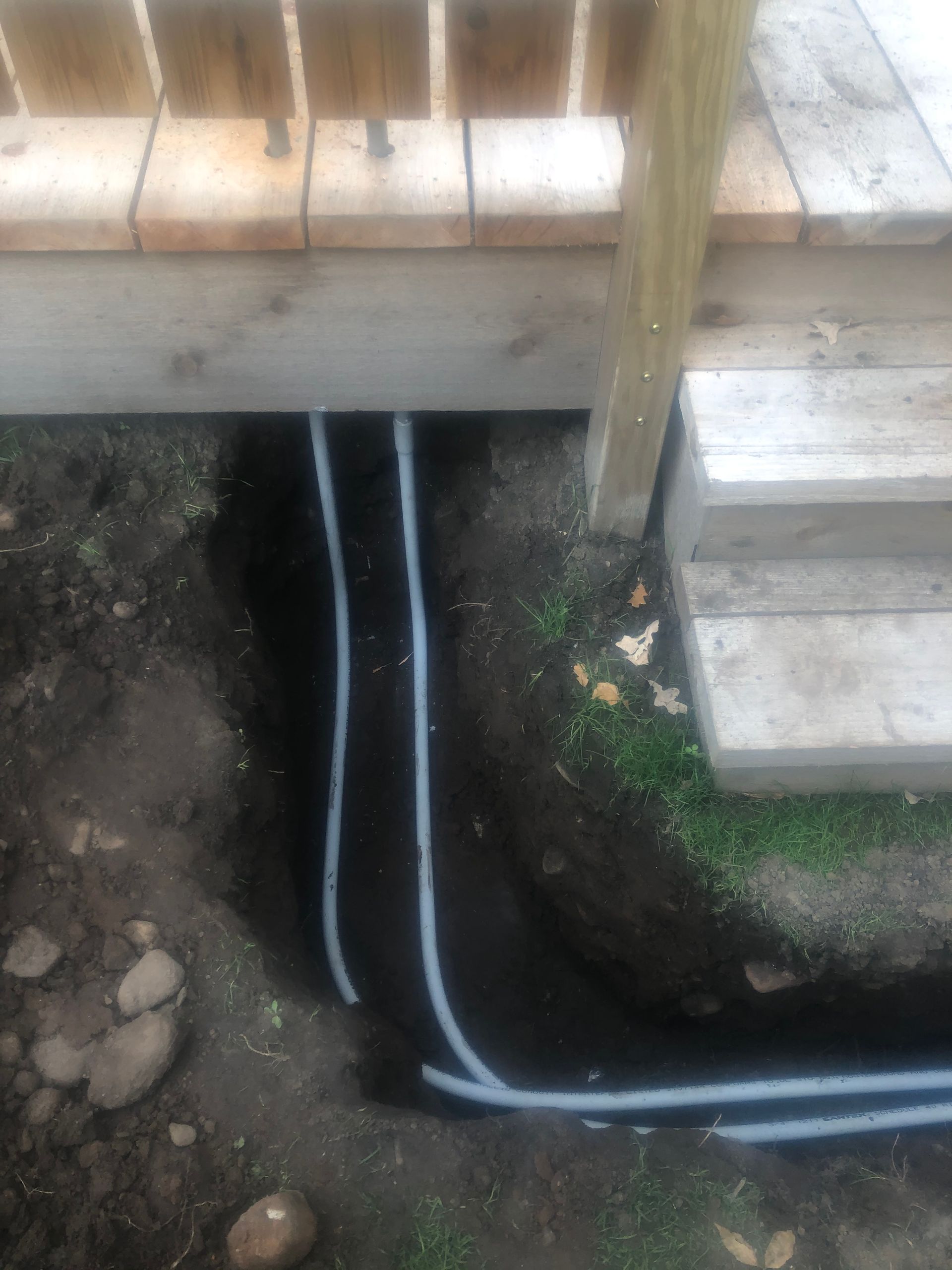 A bunch of wires are coming out of the ground under a deck.