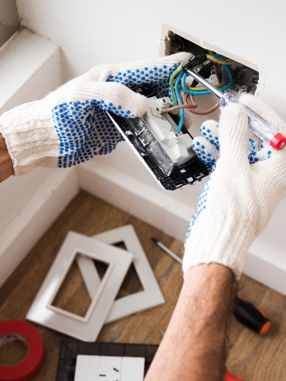 A man is working on a light switch with a screwdriver.