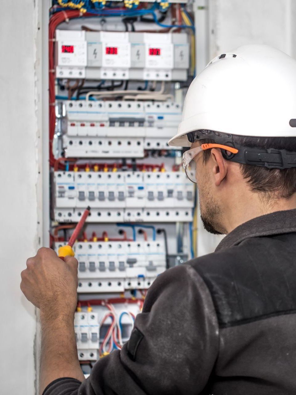 A man wearing a hard hat is working on an electrical box