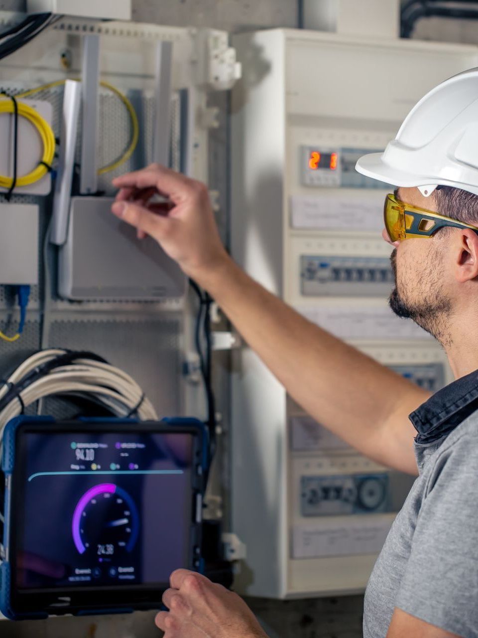 A man wearing a hard hat and goggles is using a tablet