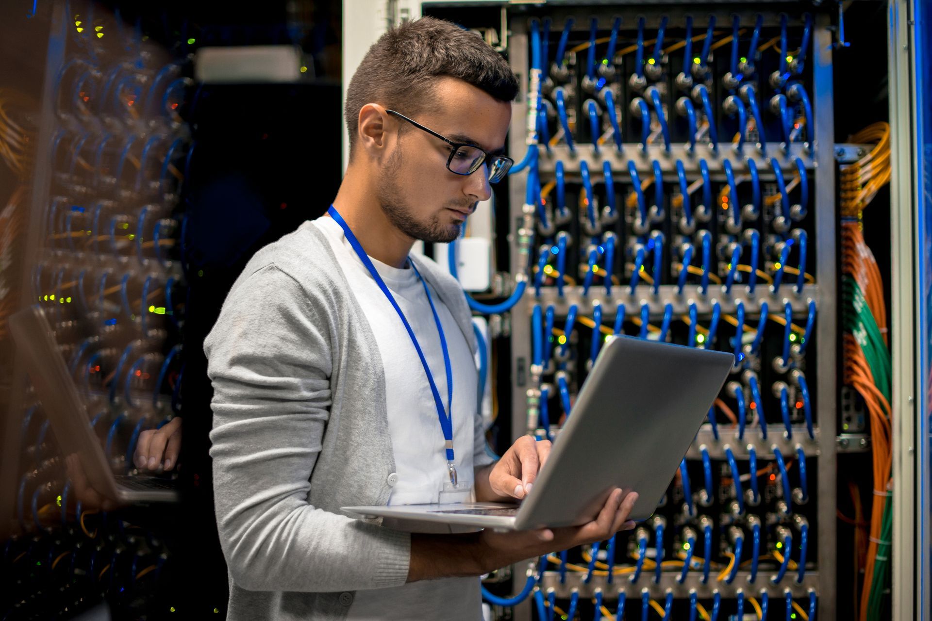 A man is using a laptop computer in a server room.