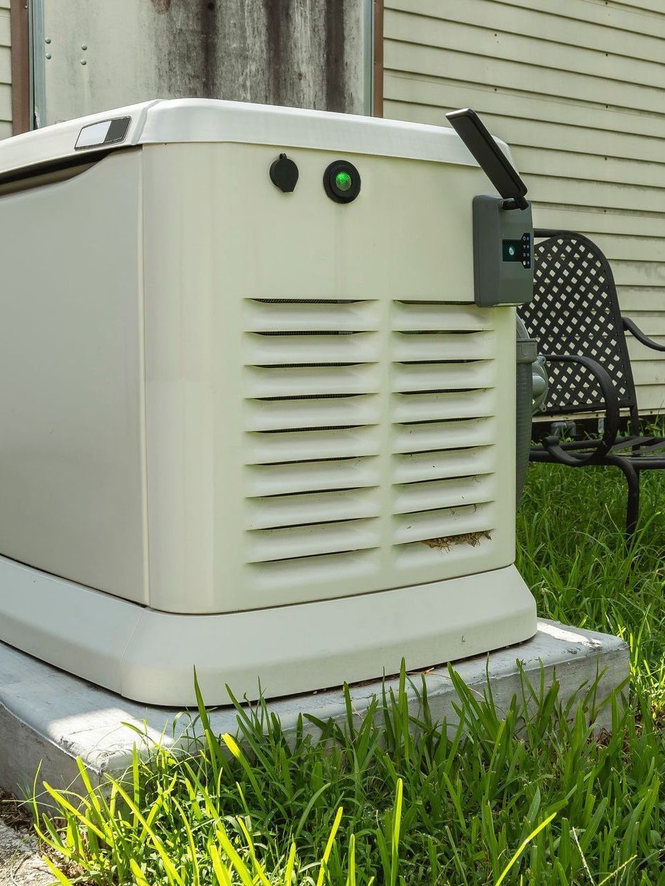 A white generator is sitting in the grass in front of a house.