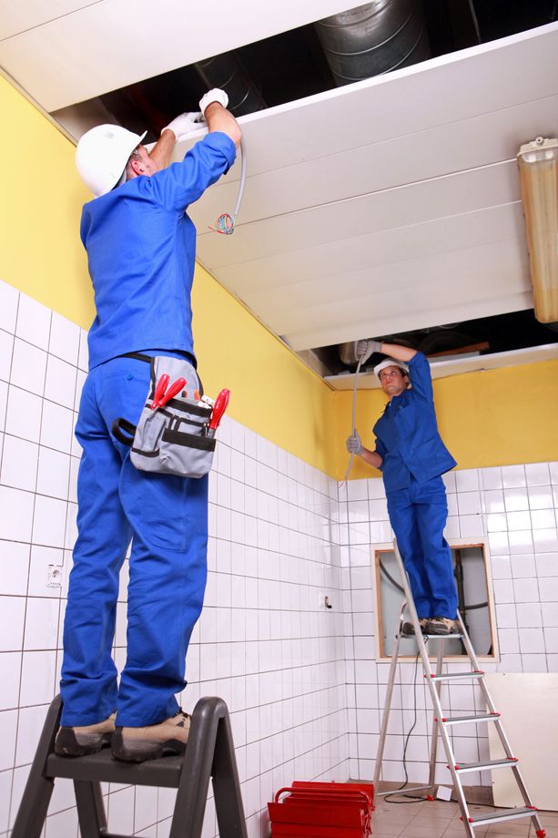 Two men are working on a ceiling in a room.