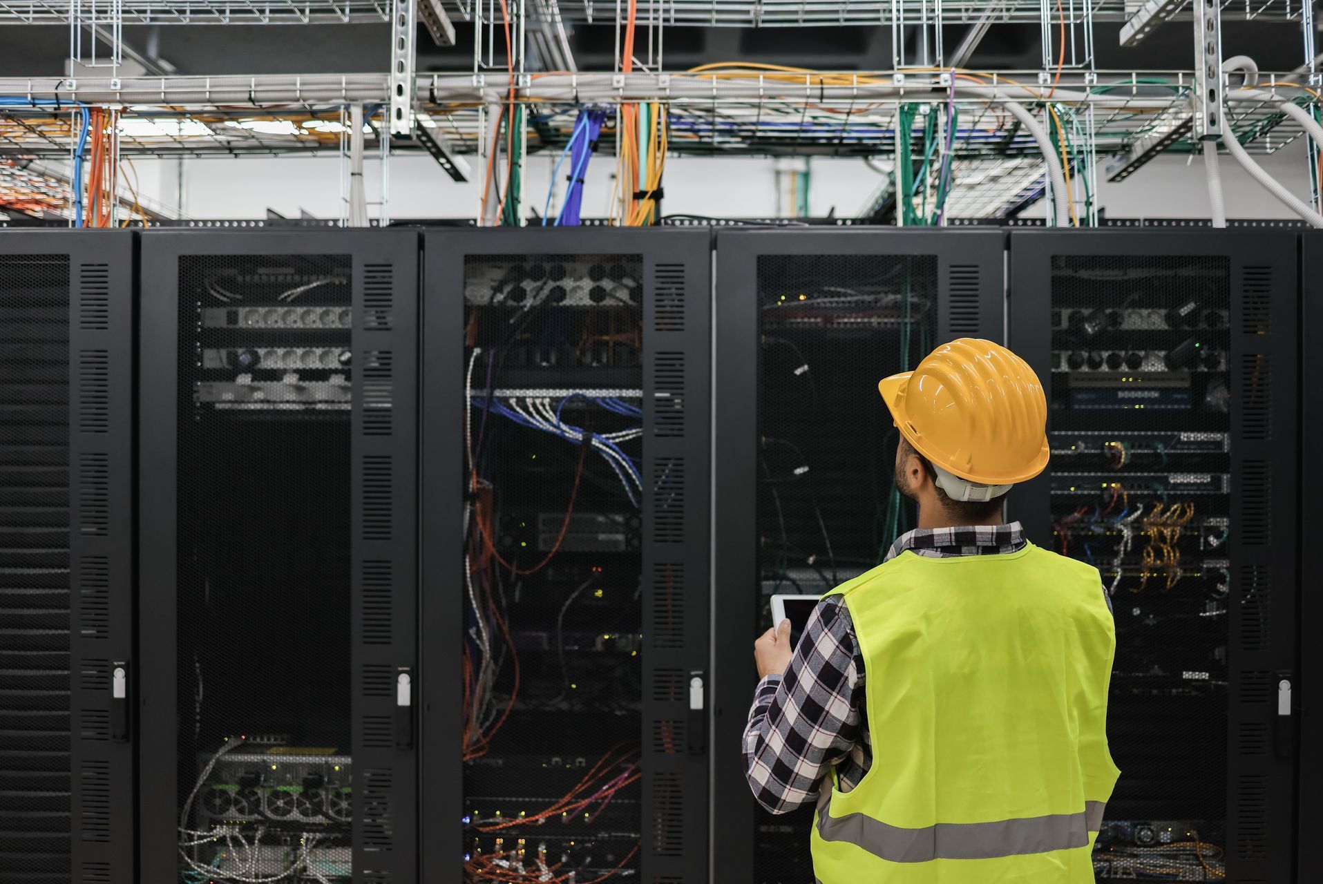 A man wearing a hard hat and a yellow vest is working on a server in a data center.