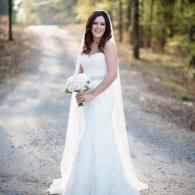 Woman in a white wedding dress holding a bouquet on a sunlit forest path