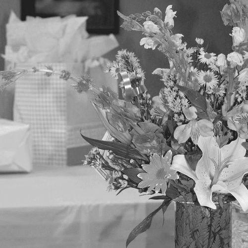Floral bouquet in a vase on a table, with wrapped gifts blurred in the background.