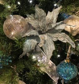 Close-up of a Christmas tree ornament with silver floral leaves, gold and blue baubles, and green branches