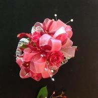Pink and red floral hair accessory with ribbon and pearl accents on a dark background