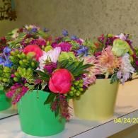 Colorful flower bouquets in green and yellow buckets on a table, with bright pink and purple blooms