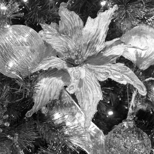 Close-up of a silver flower ornament nestled among dark tinsel and sparkling holiday decorations