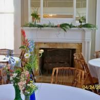 White fireplace in dining room with floral arrangements and covered round tables