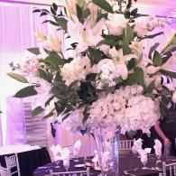 Elegant white floral centerpiece with lilies and hydrangeas in a softly lit banquet setting