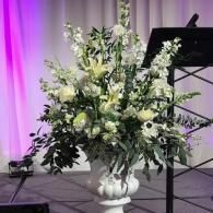 Large white floral arrangement in a vase on a stage with purple lighting