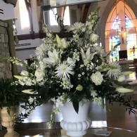 White floral arrangement in a vase inside a church interior, with stained glass in the background
