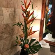 Tall floral arrangement with orange and green tropical leaves in a tiled indoor room