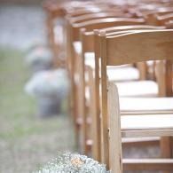 Row of light wooden chairs set outdoors along a path, with blurred greenery in the background