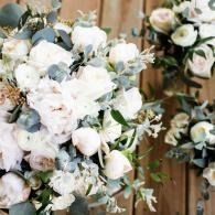 White and pale pink floral arrangement with greenery against a wooden backdrop