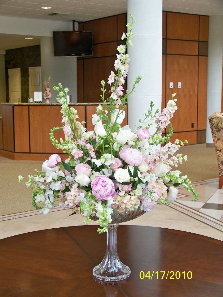 A pink-and-white floral arrangement in a glass vase on a table in a lobby with wood-paneled walls.