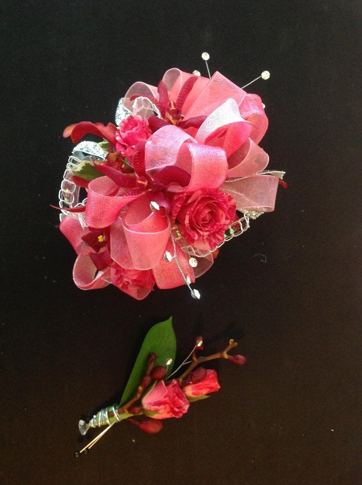 Pink floral corsage with ribbon and pearl accents, plus a matching boutonniere on a black background
