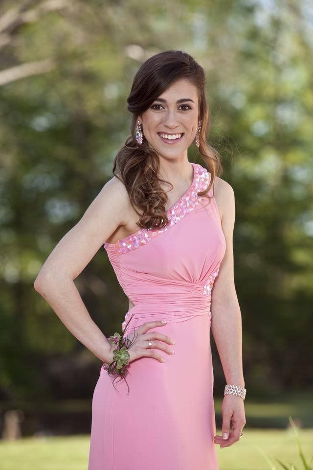 Woman in a pink dress posing outdoors, smiling with one hand on her hip.