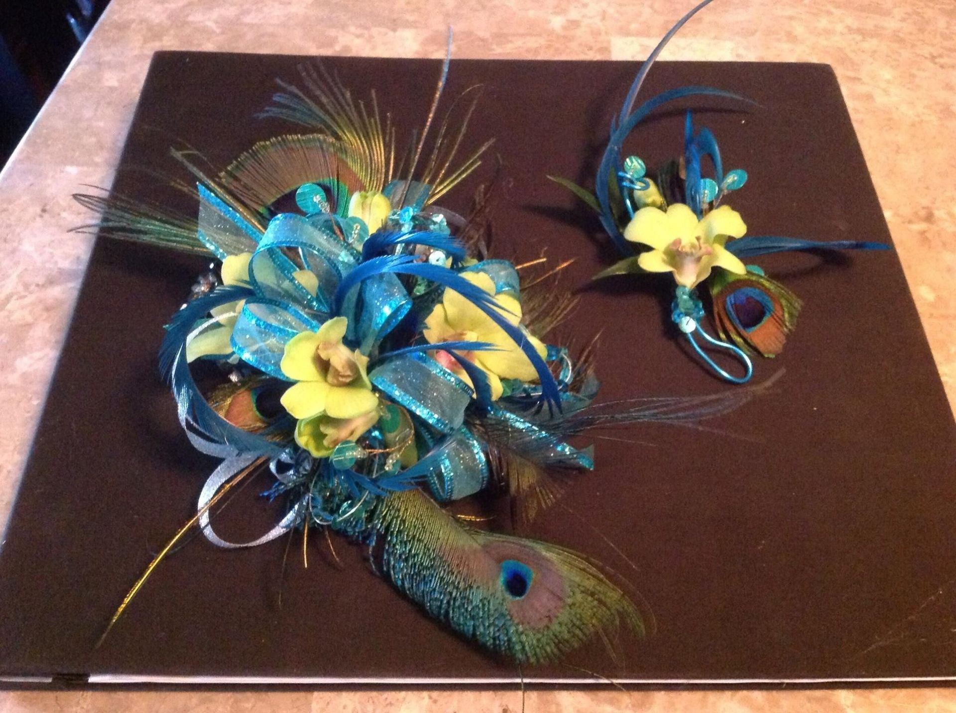 Blue and yellow decorative flower arrangement with peacock feathers on a dark card