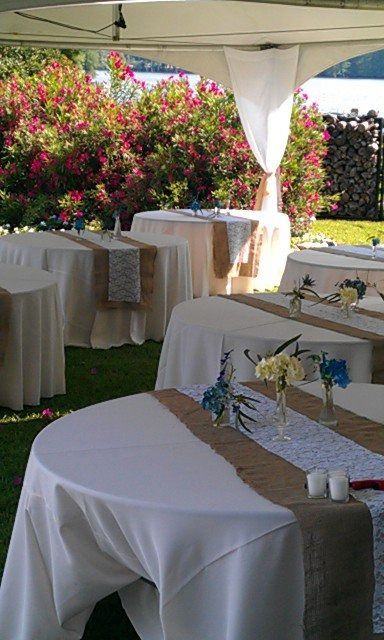 Round tables with white tablecloths and beige runners under a tent in a garden setting