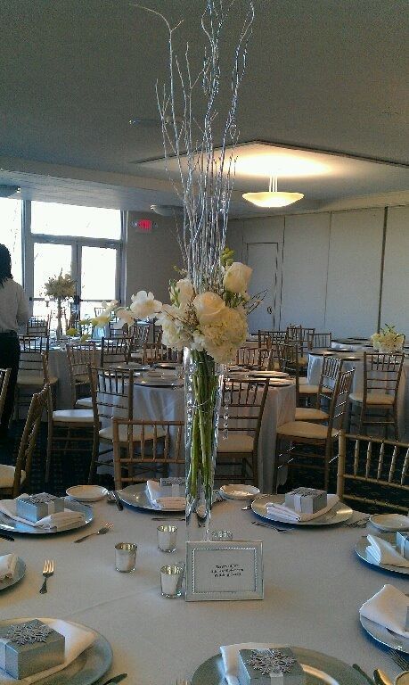 Round banquet table with white linens, silver chargers, and tall floral centerpieces in a reception hall