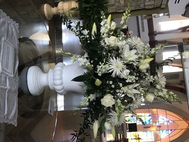 White floral arrangement in a large vase beside a stone baptismal font inside a church.