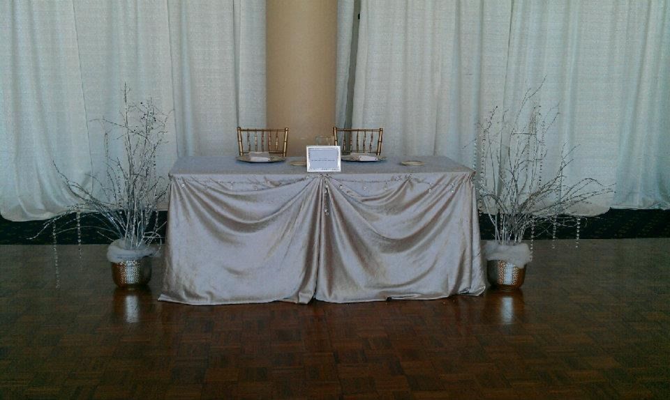 Decorative table with white drapery, candles, and branches against a curtained backdrop in a hall