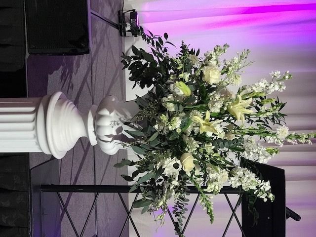 Large white floral arrangement on a pedestal beside a purple-lit stage backdrop.