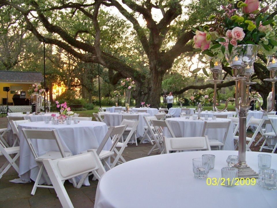 Outdoor banquet tables with white tablecloths and pink floral centerpieces under trees at sunset