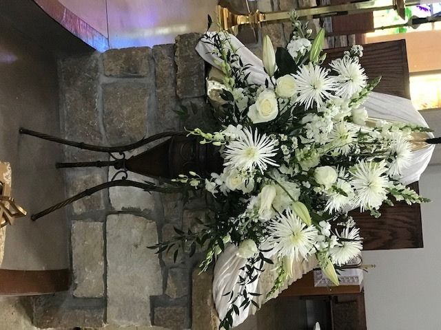 White floral arrangement on a black stand displayed indoors beside a stone wall.