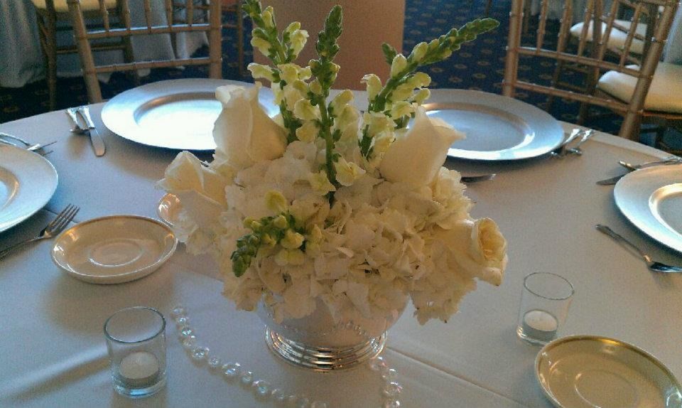 White floral centerpiece on a round banquet table set with plates, glassware, and silver napkins