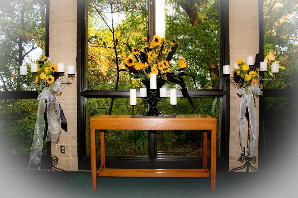 Sunflower memorial arrangement on a wooden table between two window displays with wreaths and candles