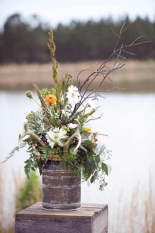 Wildflower bouquet in a rustic metal bucket on a wooden table by a lake