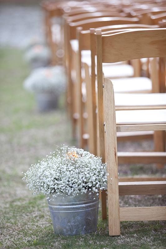 Row of wooden chairs on grass with small white flowers in a gray metal bucket in the foreground
