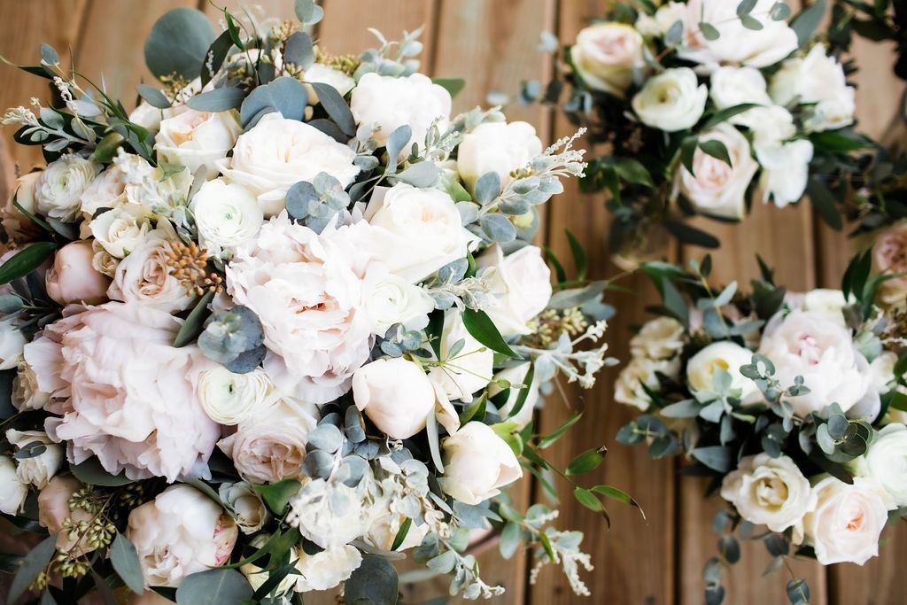 White and pale pink floral arrangements with greenery on a wooden background