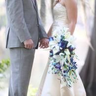 Bride and groom holding hands, with the bride’s white dress and blue-white cascading bouquet visible.