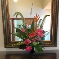 Pink and orange floral arrangement in a vase on a dark table before a framed mirror