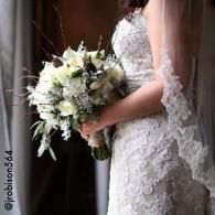 Bride in a lace wedding dress holding a white bouquet by a window