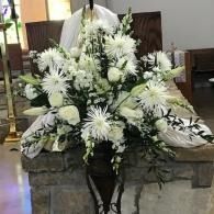 White floral funeral arrangement with lilies and greenery on a stone altar